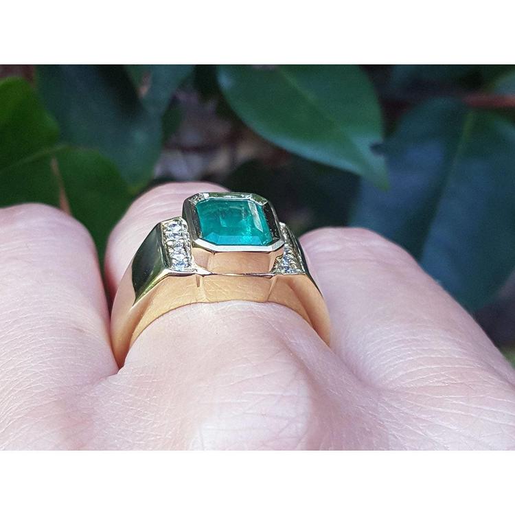 Gold ring for men with accent natural diamond on a finger against a leafy background.