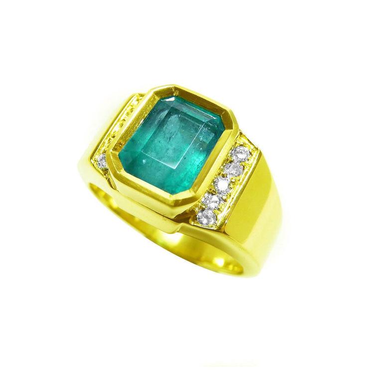 A natural emerald ring for men yellow gold with accent diamonds on a tilted position displaying its topside and band profile.