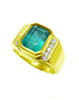 A natural emerald ring for men yellow gold with accent diamonds on a tilted position displaying its topside and band profile.