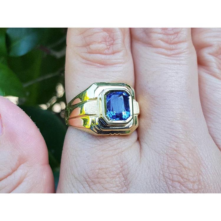 Gold ring with a blue natural sapphire gemstone on a hand against a blurred green background
