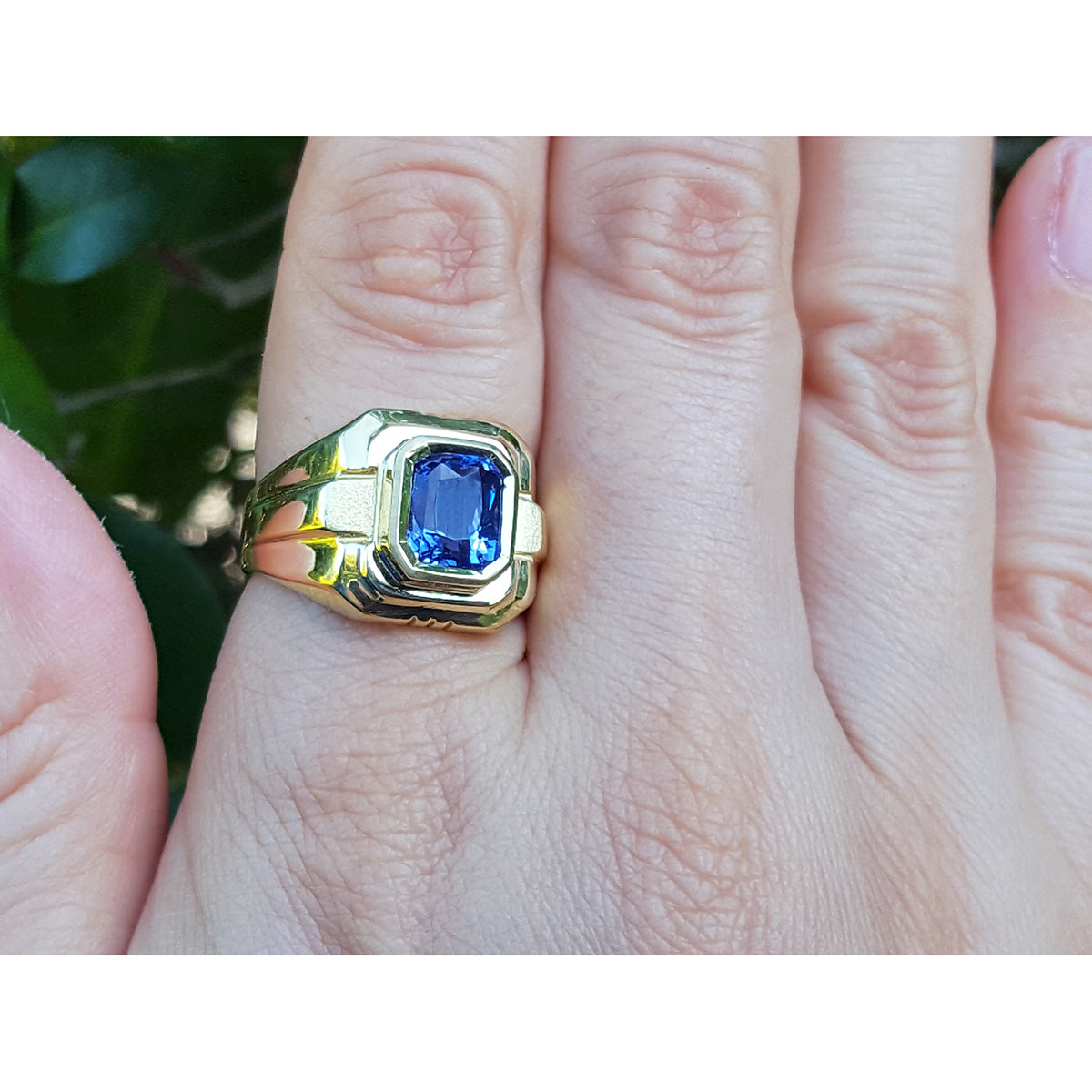 Gold ring with a blue natural sapphire gemstone on a hand against a natural background