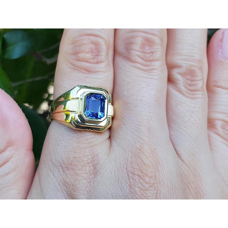 Gold ring with a blue natural sapphire gemstone on a hand against a natural background