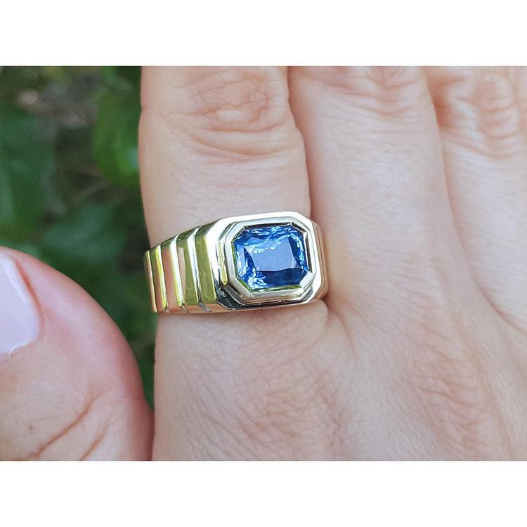 Gold ring with a blue natural blue sapphire gemstone on a hand against a blurred green background