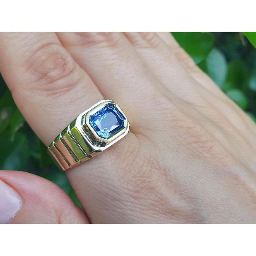 Men's 18k yellow gold ring with a vibrant blue octagonal emerald cut sapphire, bezel set east-west.