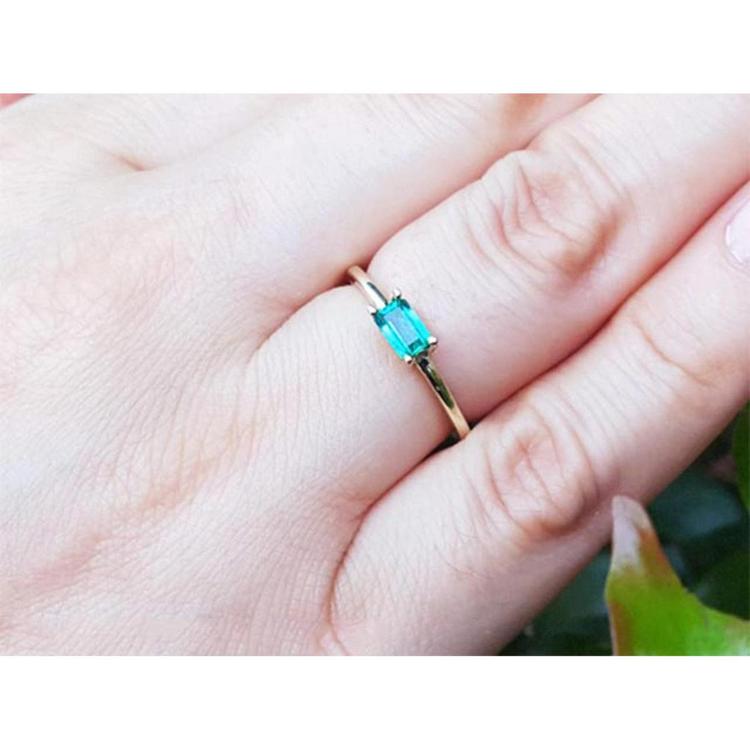 A 14k yellow gold minimalist natural emerald solitaire ring on a person's finger.