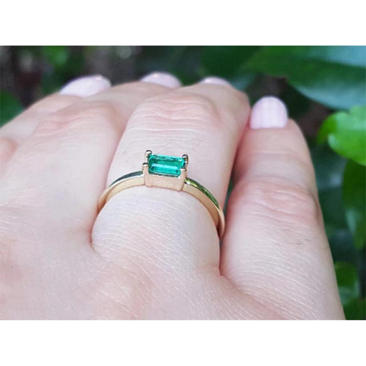 A yellow gold emerald ring on a hand against a blurred natural background