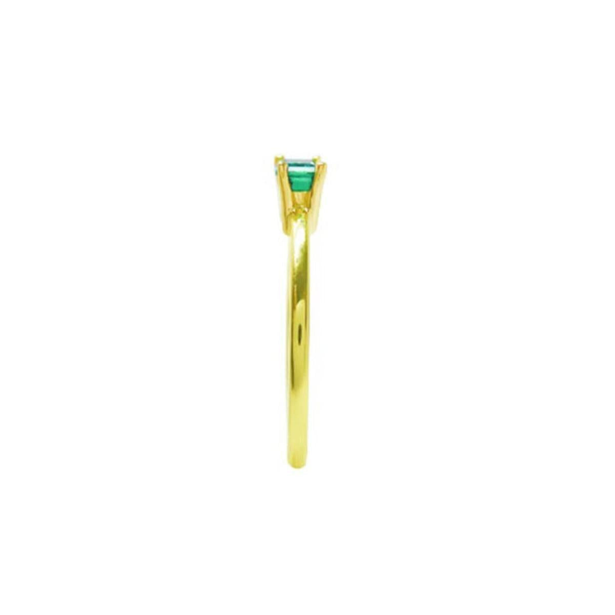 The side position of a minimalist solitaire emerald ring in yellow gold.
