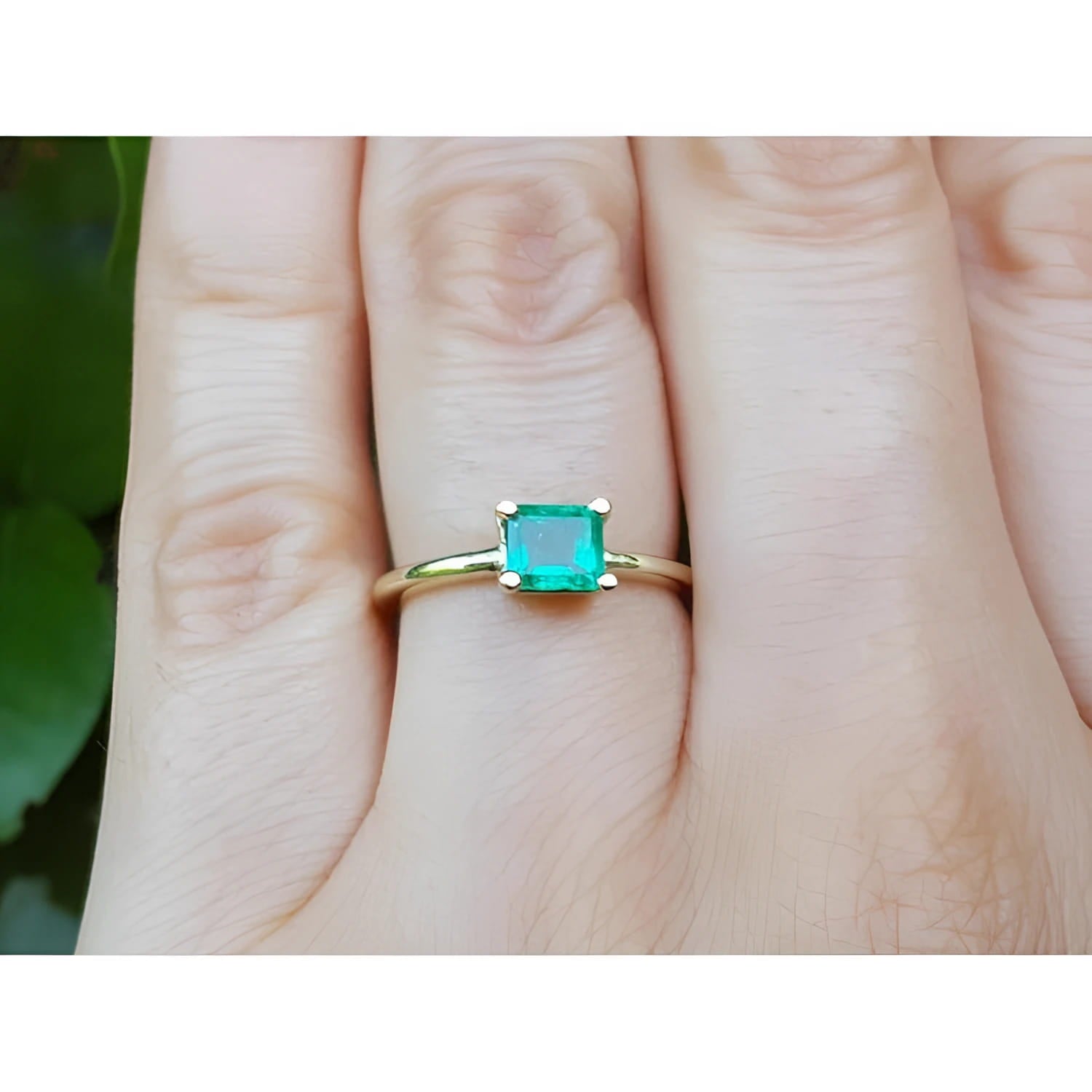 A minimalist emerald solitaire ring in 14k gold representing May's birthstone jewelry on a hand.