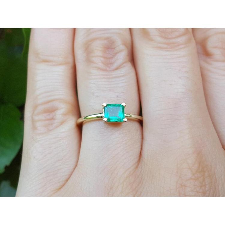 A minimalist emerald solitaire ring in 14k gold representing May's birthstone jewelry on a hand.