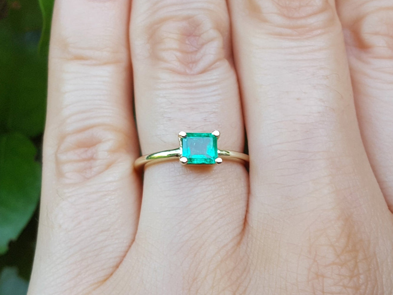 Tis minimalist emerald solitaire ring representing May's birthstone jewelry on a hand against a natural background