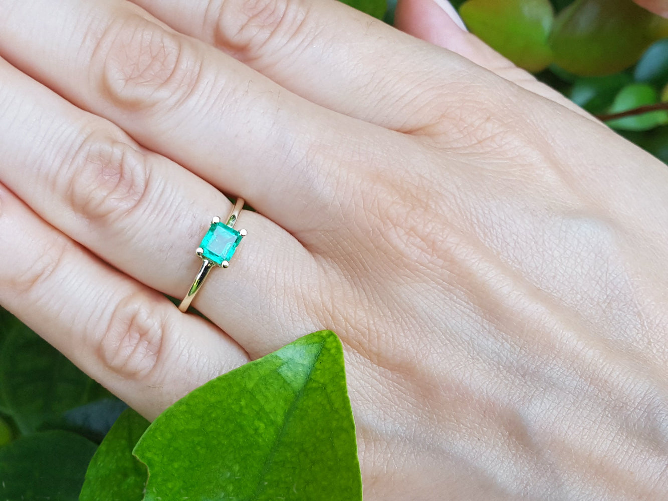 Emerald gold ring on a hand with a green leaf background.