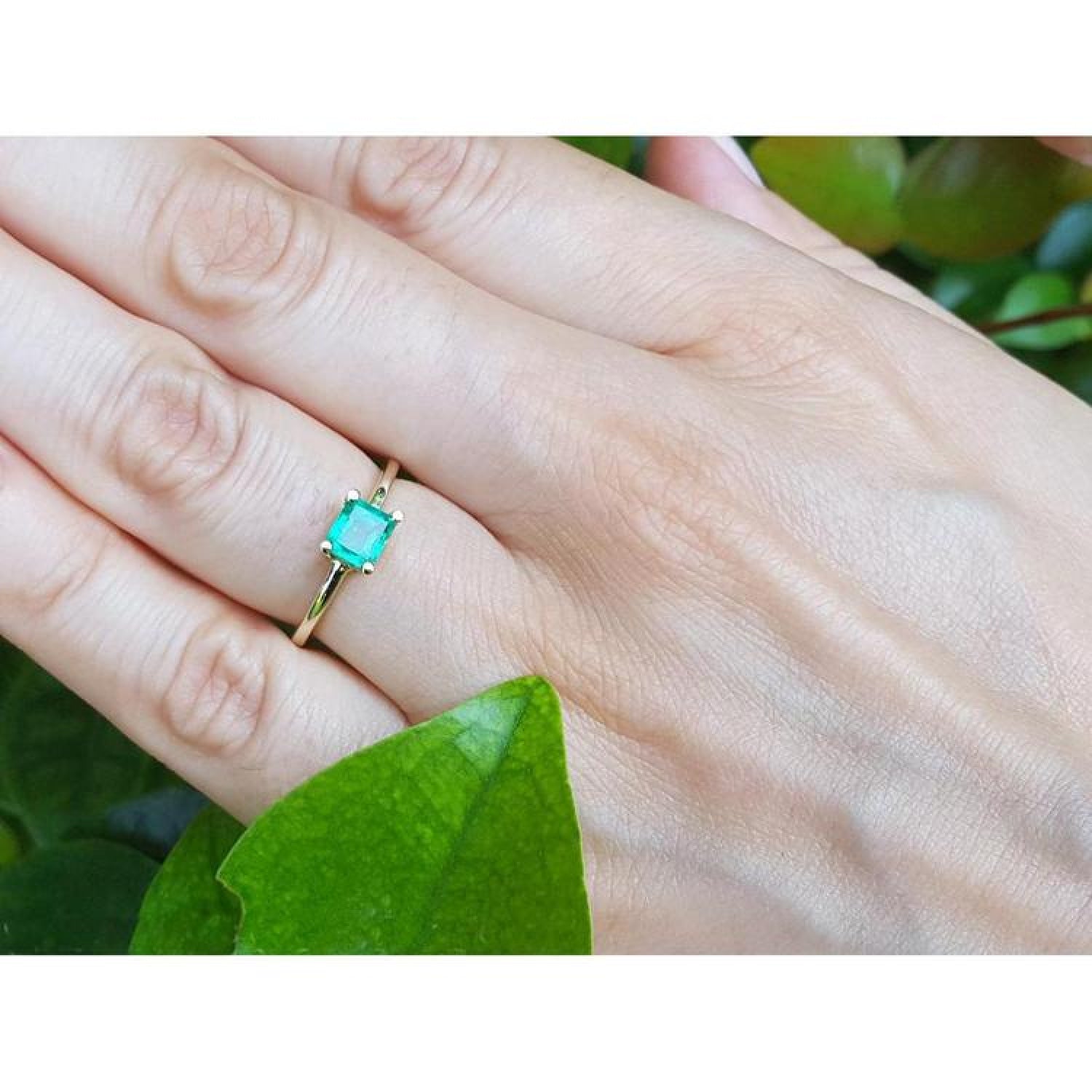 Minimalist 14K yellow gold solitaire ring with a square-cut green emerald on a hand.