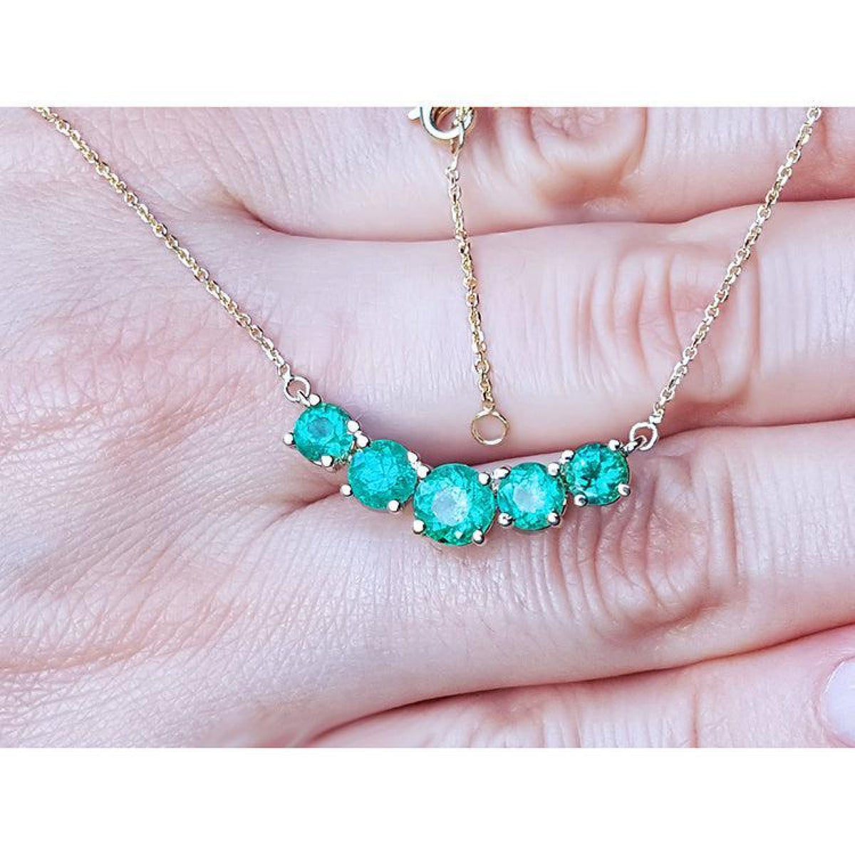 14K gold necklace with five round, medium green Colombian emeralds in elegant basket settings.