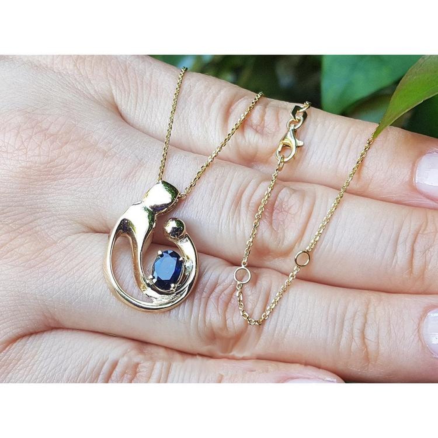 14K yellow gold mother and child pendant necklace with an oval blue sapphire, held by a hand.