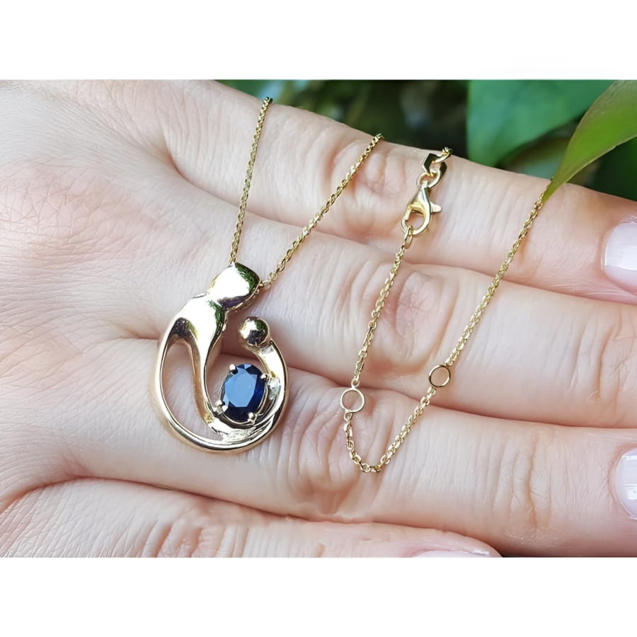 14K yellow gold mother and child pendant necklace with an oval blue sapphire, held by a hand.