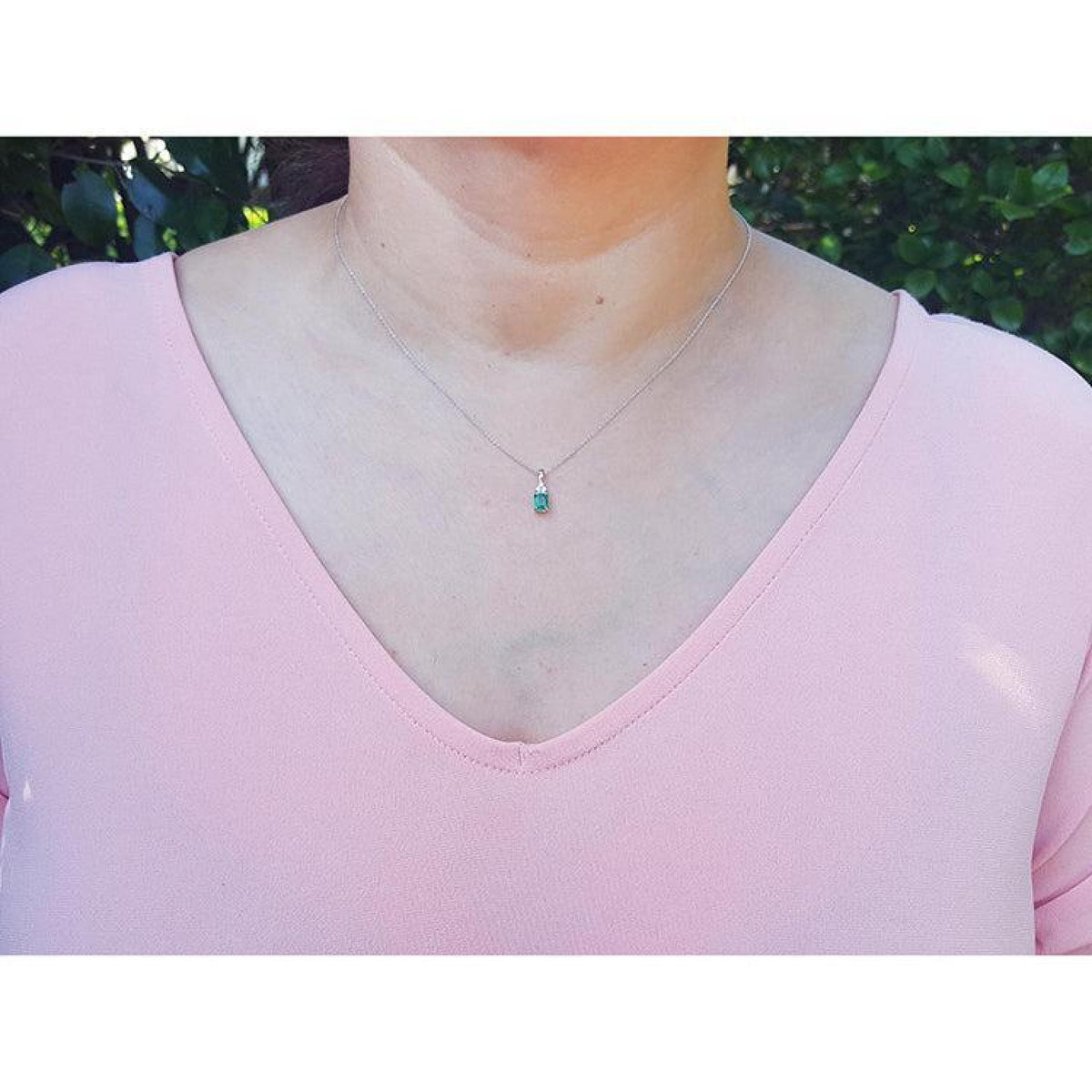 0.27 ct Colombian emerald pendant in 14K white gold, worn on a woman's neck over a pink top.