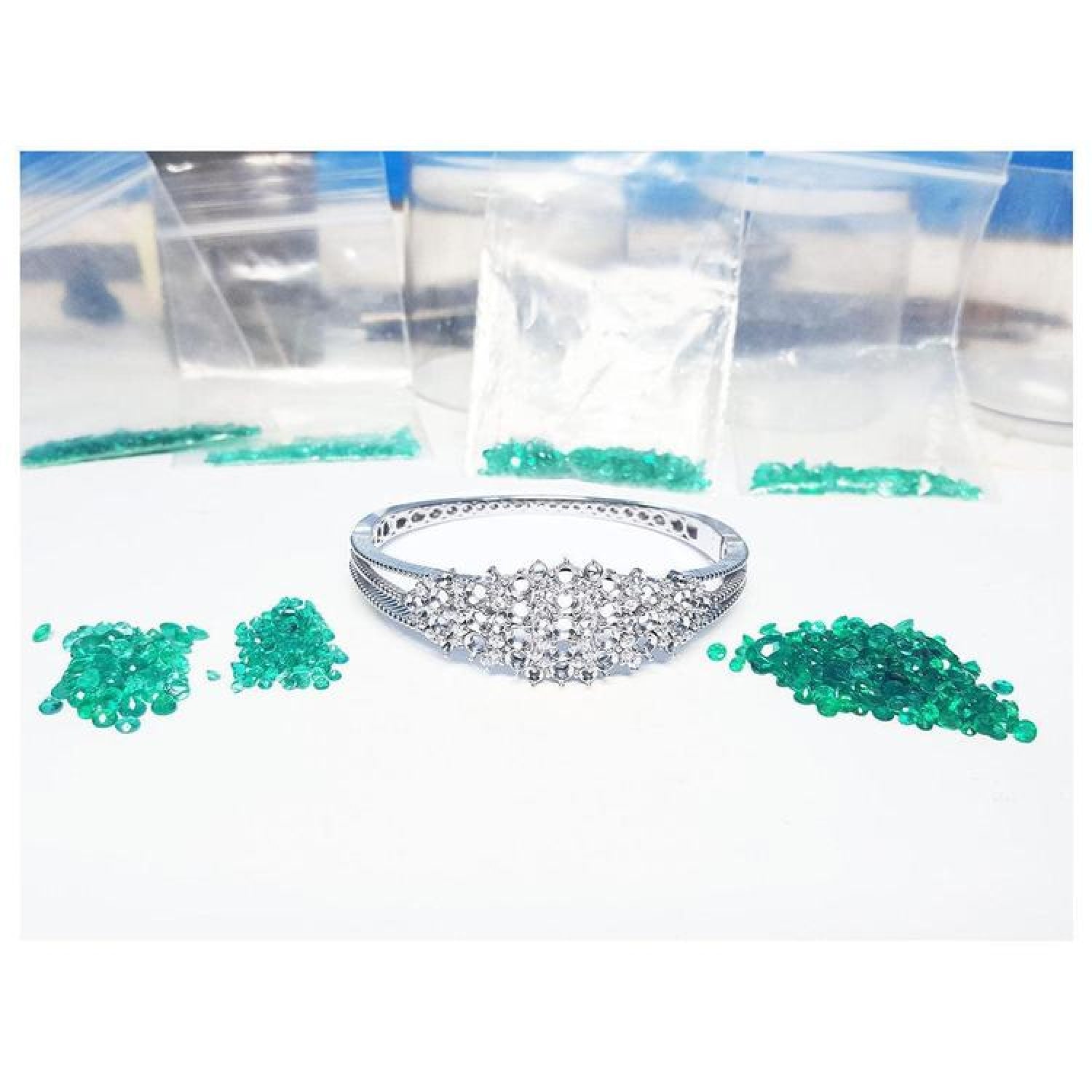White gold bangle bracelet with diamonds, surrounded by loose green Colombian emeralds and small bags.