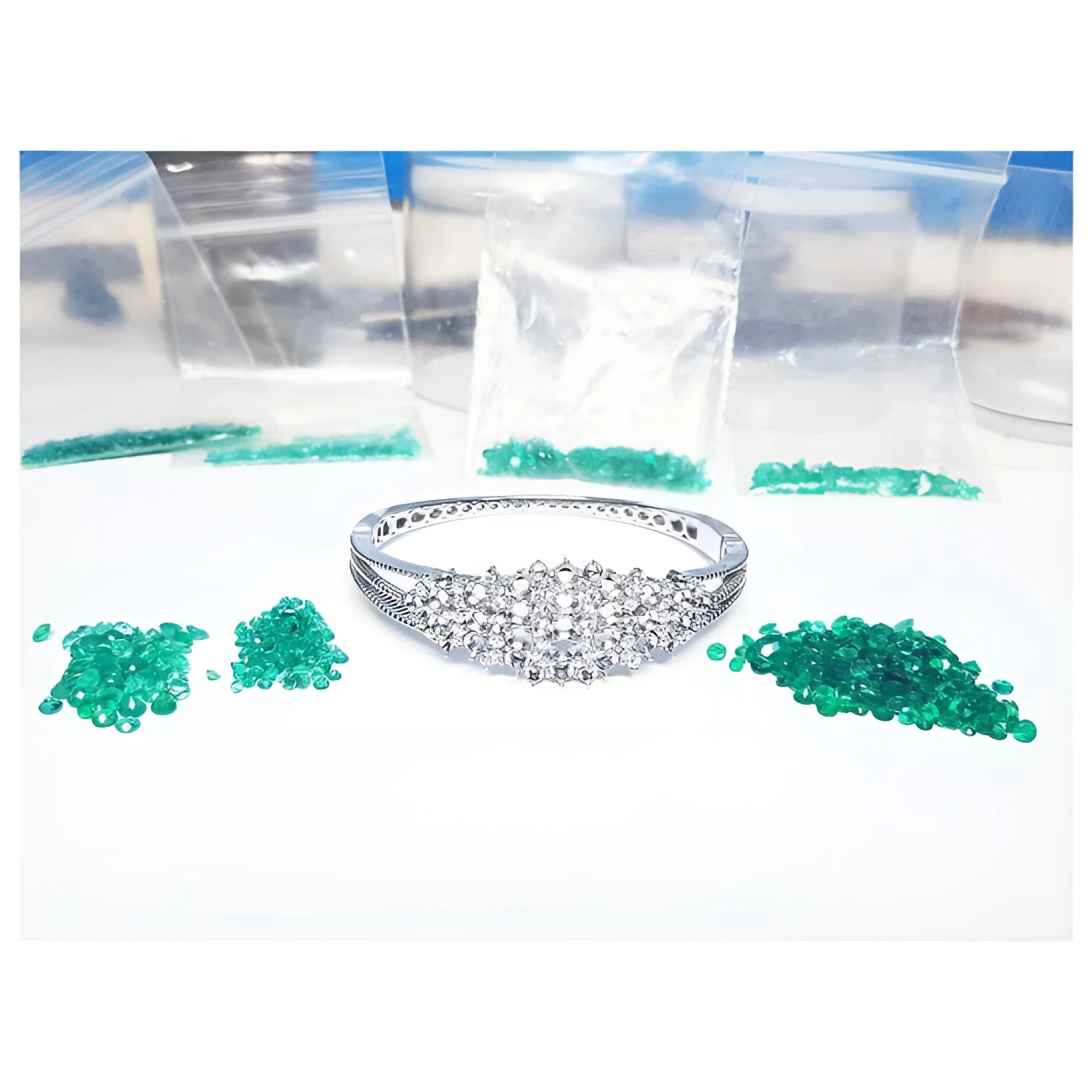 White gold bangle bracelet with diamonds, surrounded by loose green Colombian emeralds and small bags.