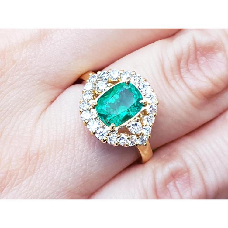 A cushion cut Muzo colombian emerald surrounded by a halo diamond 14k gold ring on a person's finger.