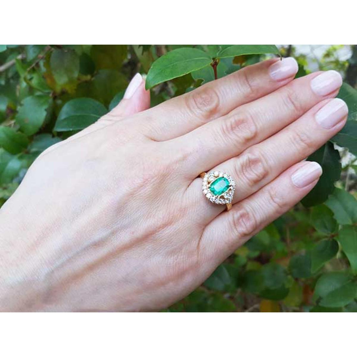 Hand wearing an emerald ring with a green leafy background.