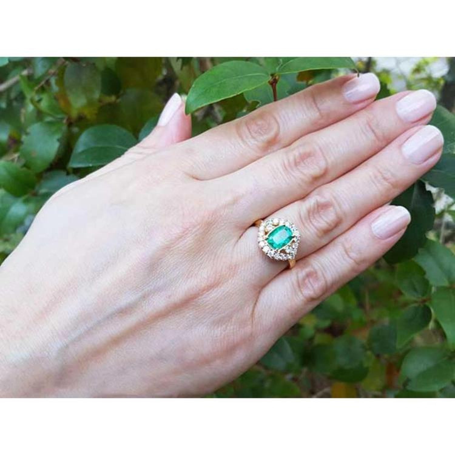 1.43 ct cushion-cut Muzo Colombian emerald ring with marquise diamond halo in 14K yellow gold on a hand.