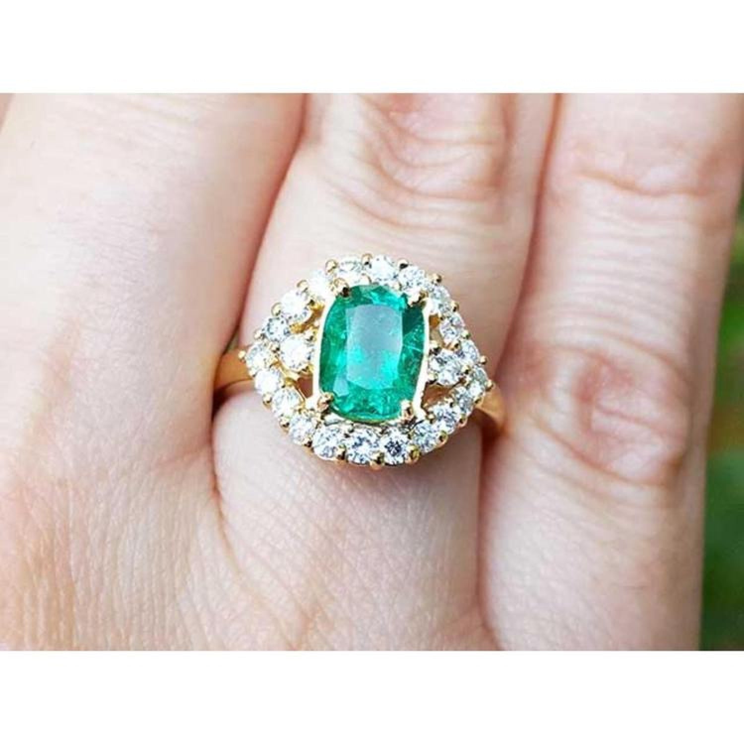1.43 ct cushion-cut Muzo Colombian emerald ring with diamond halo in 14K yellow gold on a finger.