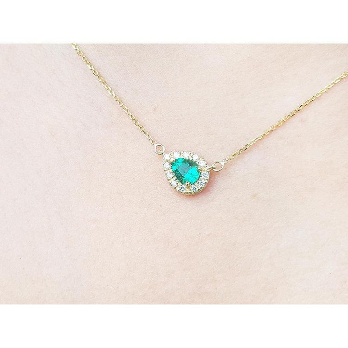 Vibrant pear-shaped emerald necklace with diamond halo on a delicate 14K yellow gold chain.