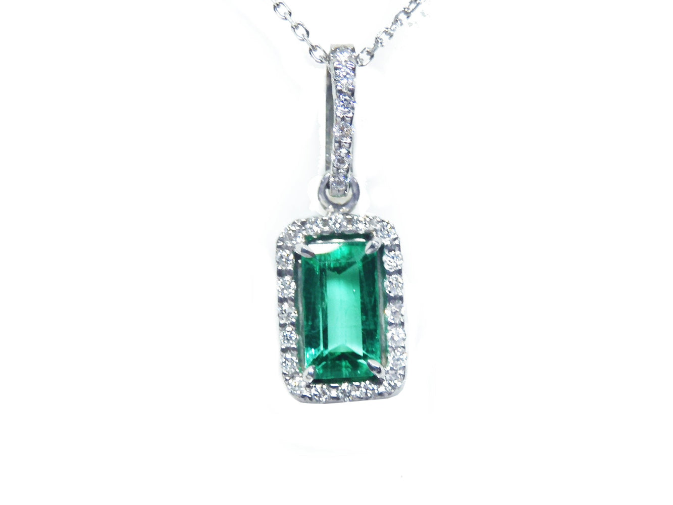 Natural Muzo emerald pendant with diamond accents on a topside view.
