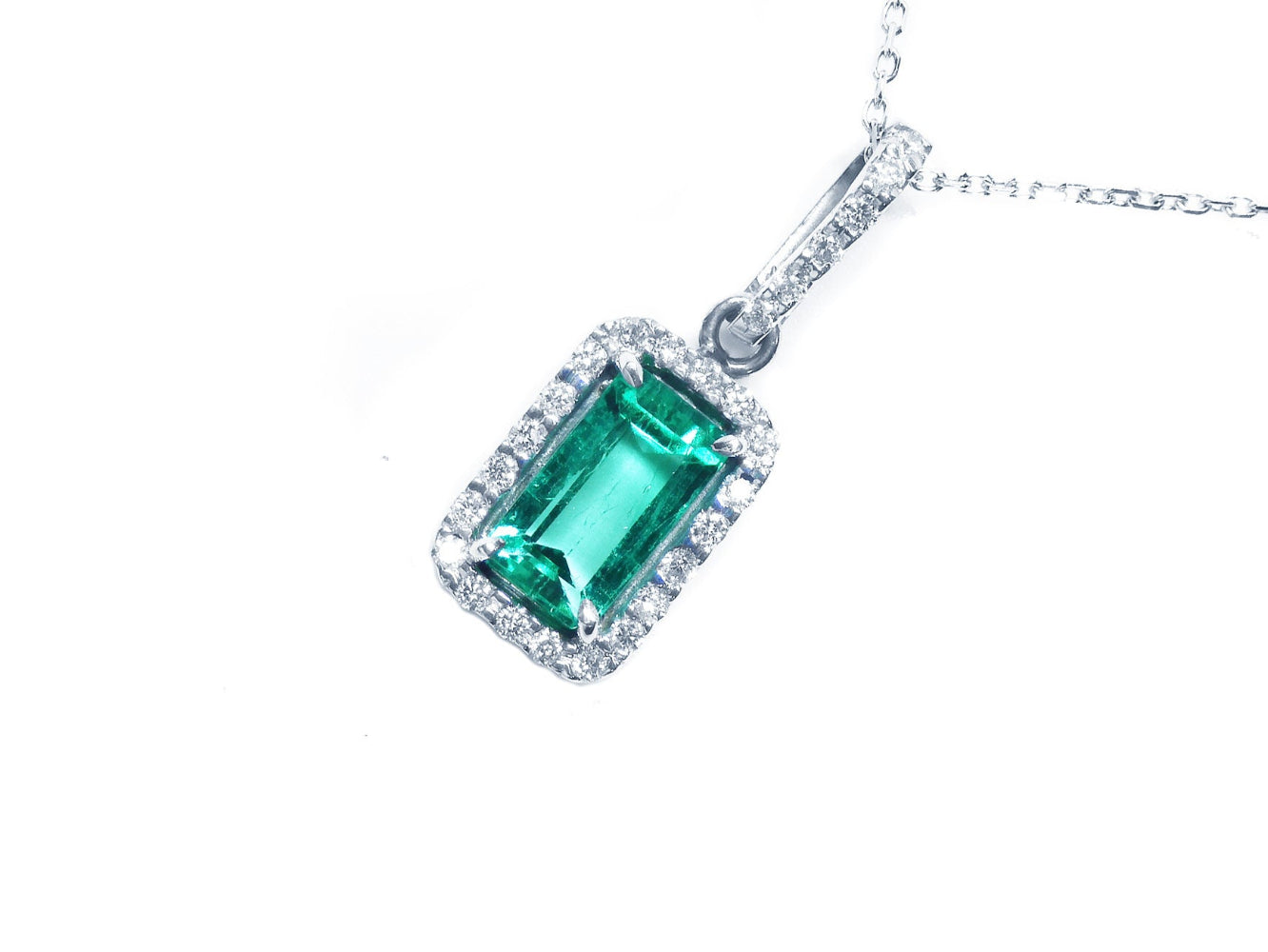 Emerald green gemstone pendant with diamond accents on a white background