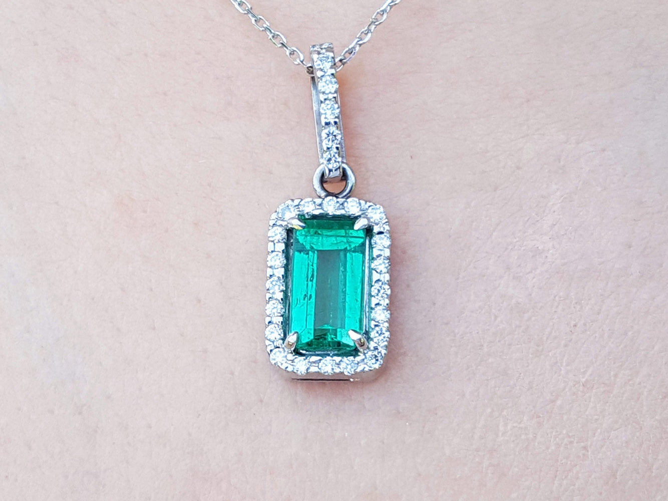 White gold emerald pendant with diamond accents on a light pink skin background.