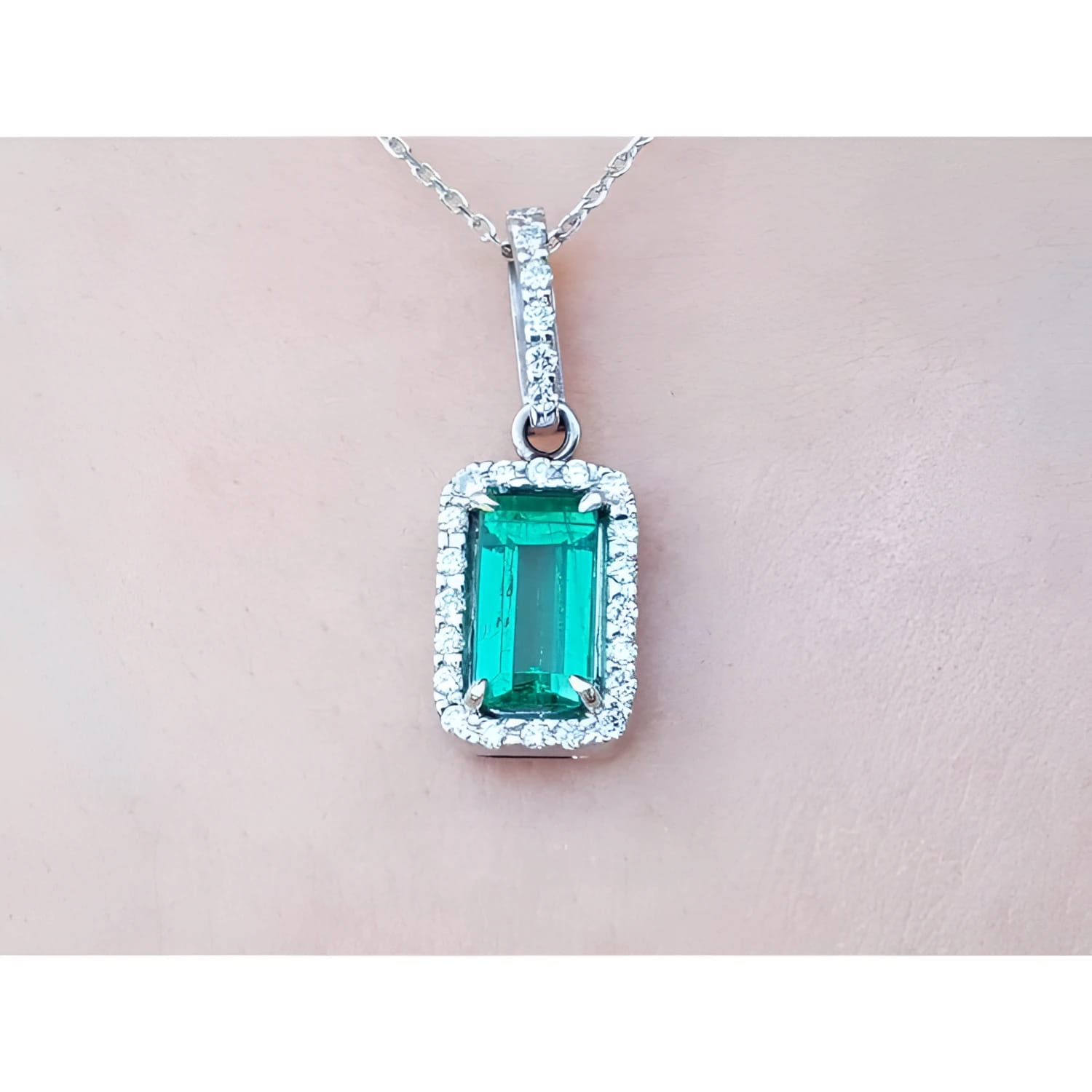 White gold emerald pendant with diamond accents on a light pink skin background.