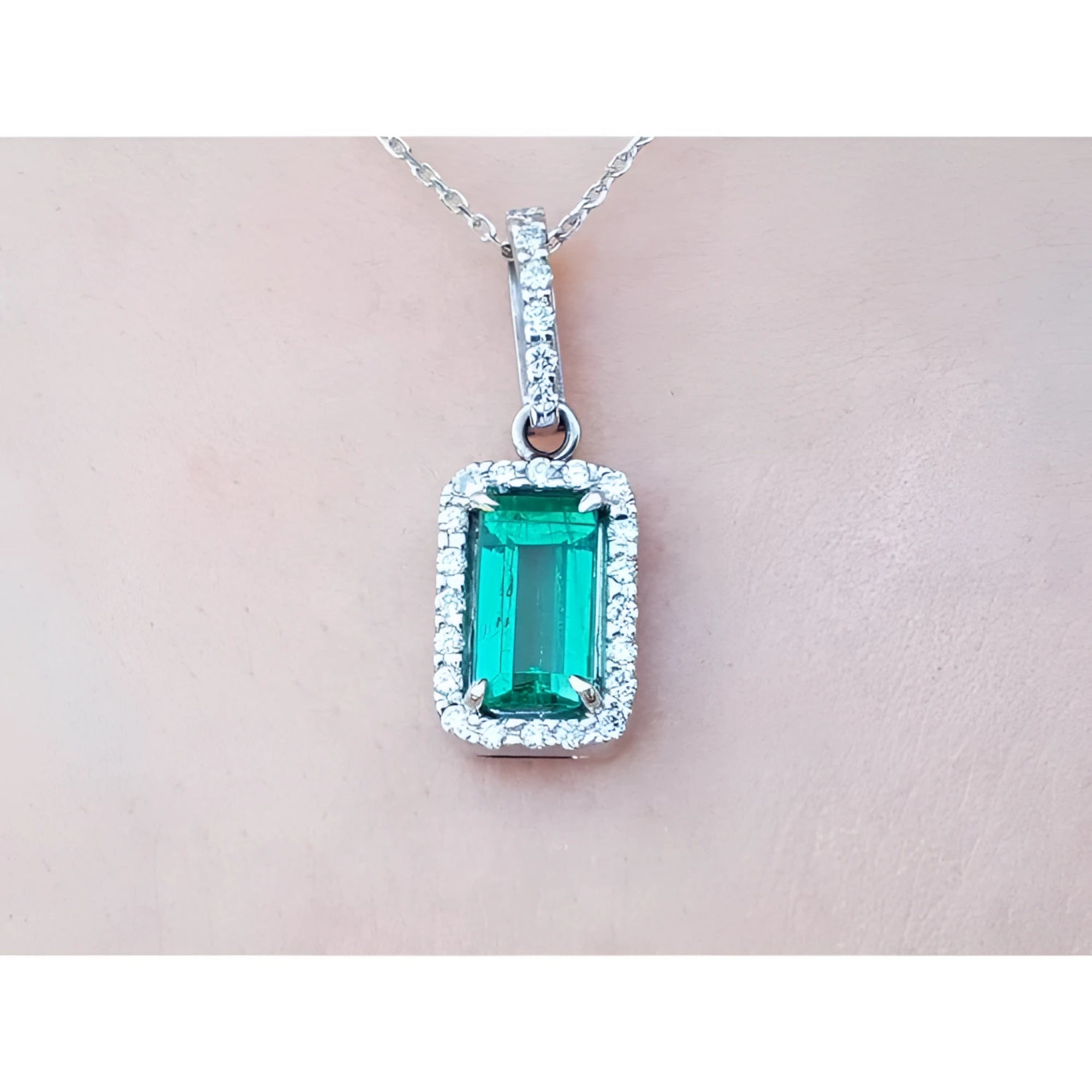 White gold emerald pendant with diamond accents on a light pink skin background.