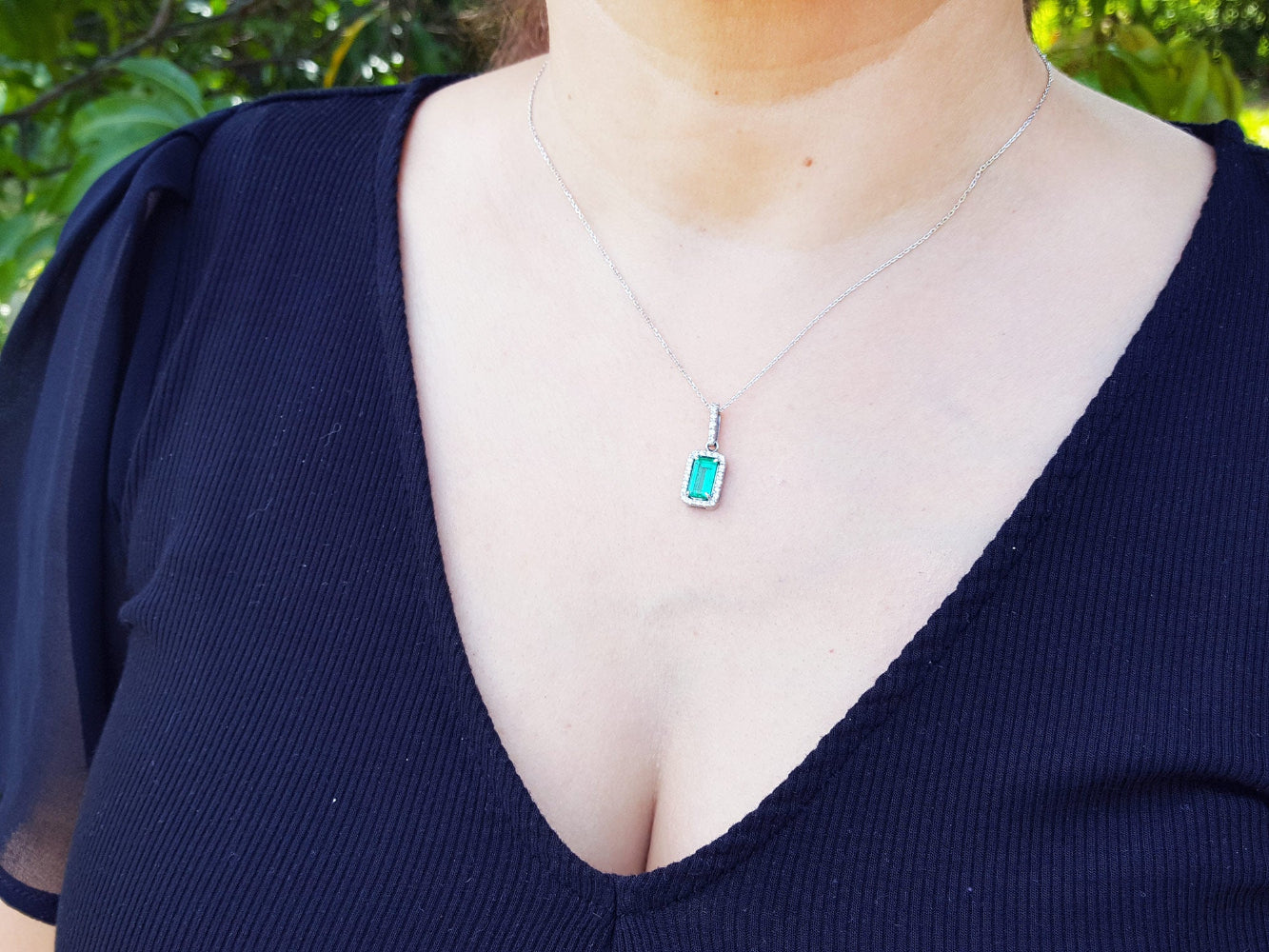A woman wearing a natural Muzo colombian emerald pendant against a green leafy background.