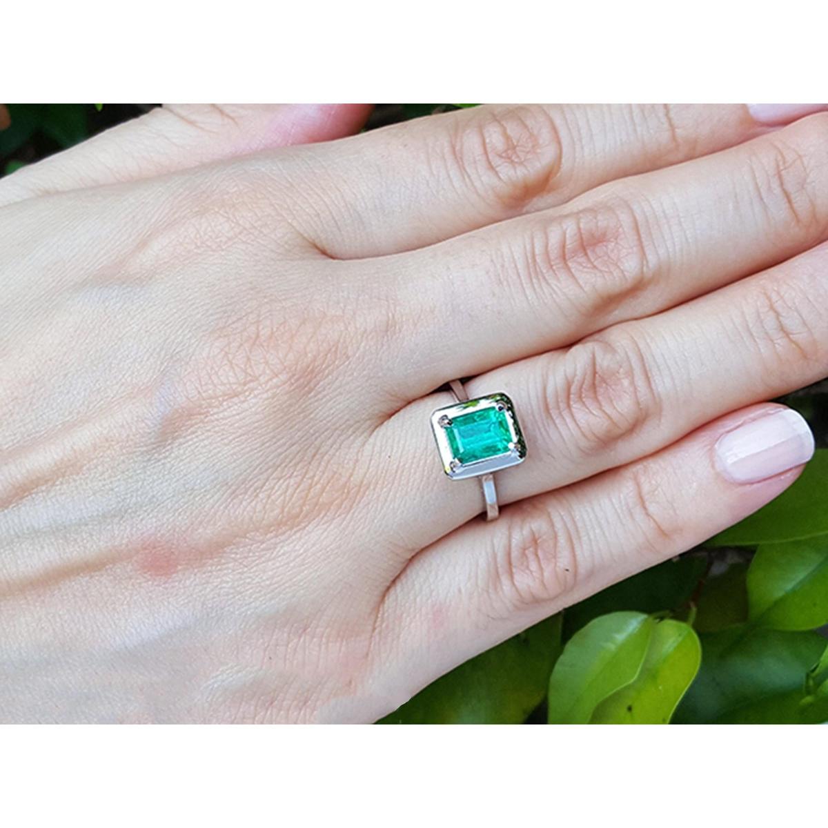 Hand wearing a white gold ring with a natural emerald gemstone against a natural background
