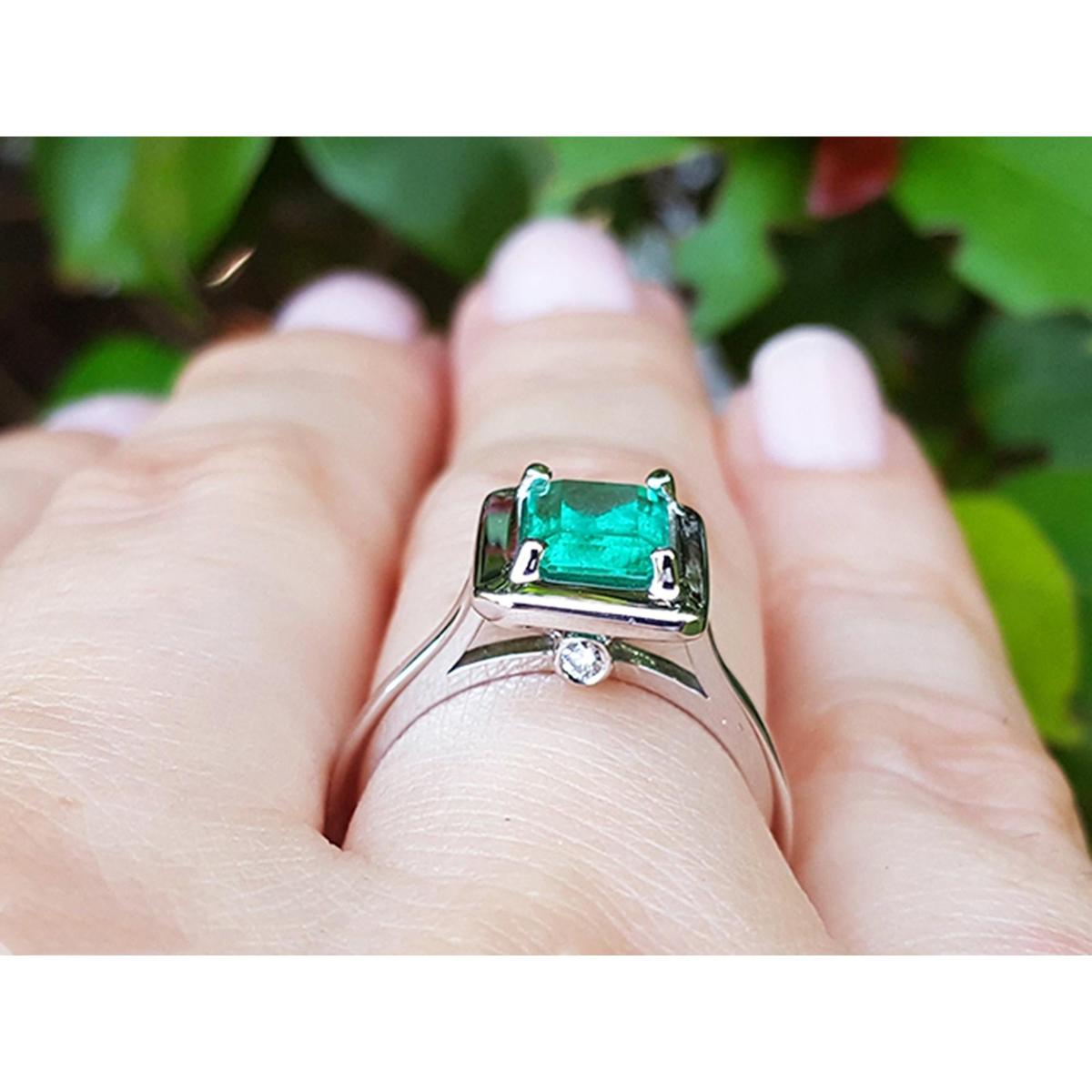 White gold ring with a natural emerald gemstone on a hand against a blurred green leafy background