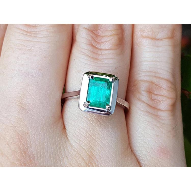 A solitaire Muzo colombian emerald solitaire ring in 18k white gold on a person's finger.