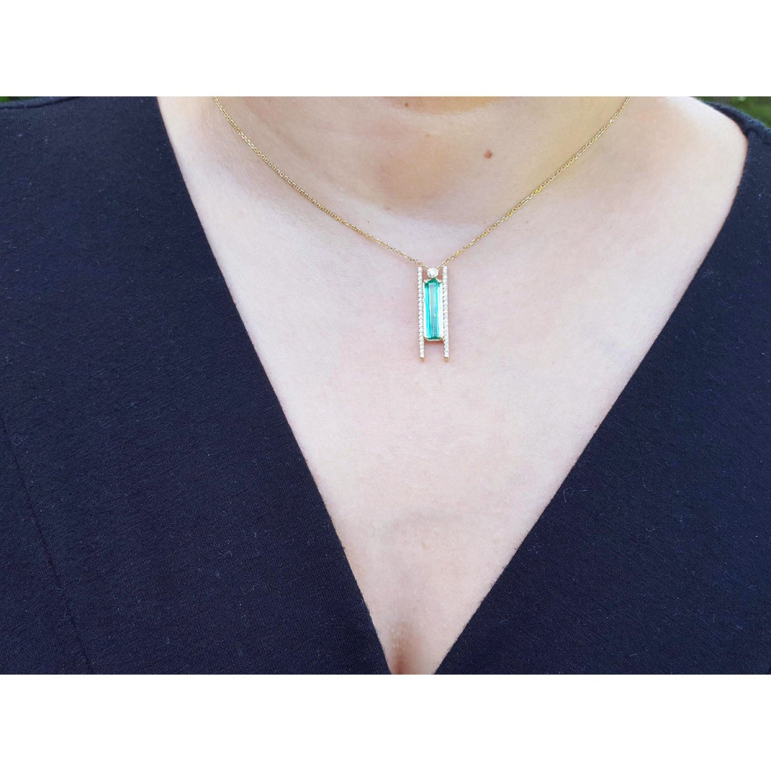 Emerald baguette cut necklace with natural diamonds, 14K yellow gold, worn on a person styled against a black V-neck top.