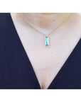 Emerald baguette cut necklace with natural diamonds, 14K yellow gold, worn on a person styled against a black V-neck top.