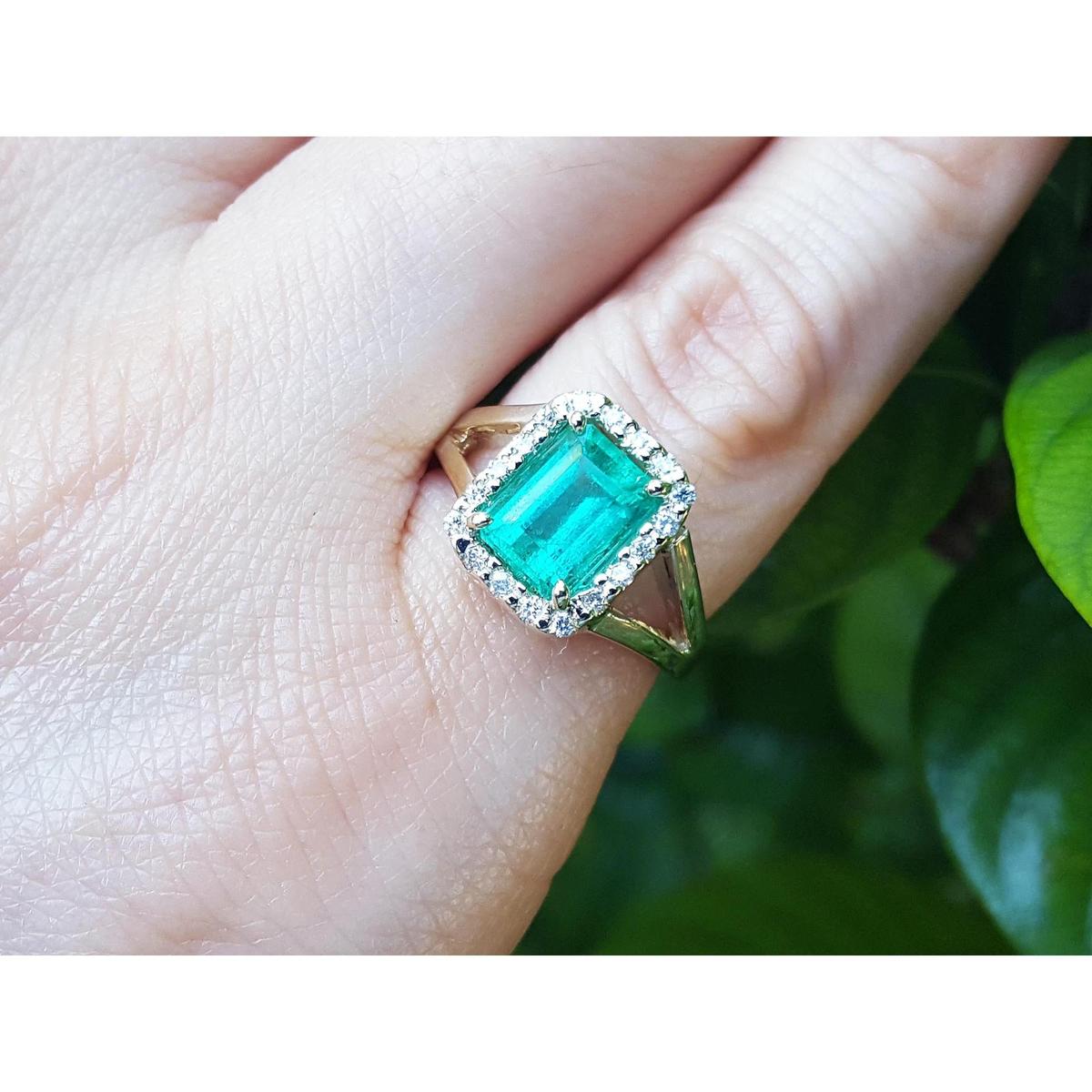 An emerald-cut emerald ring on a hand with a natural background.