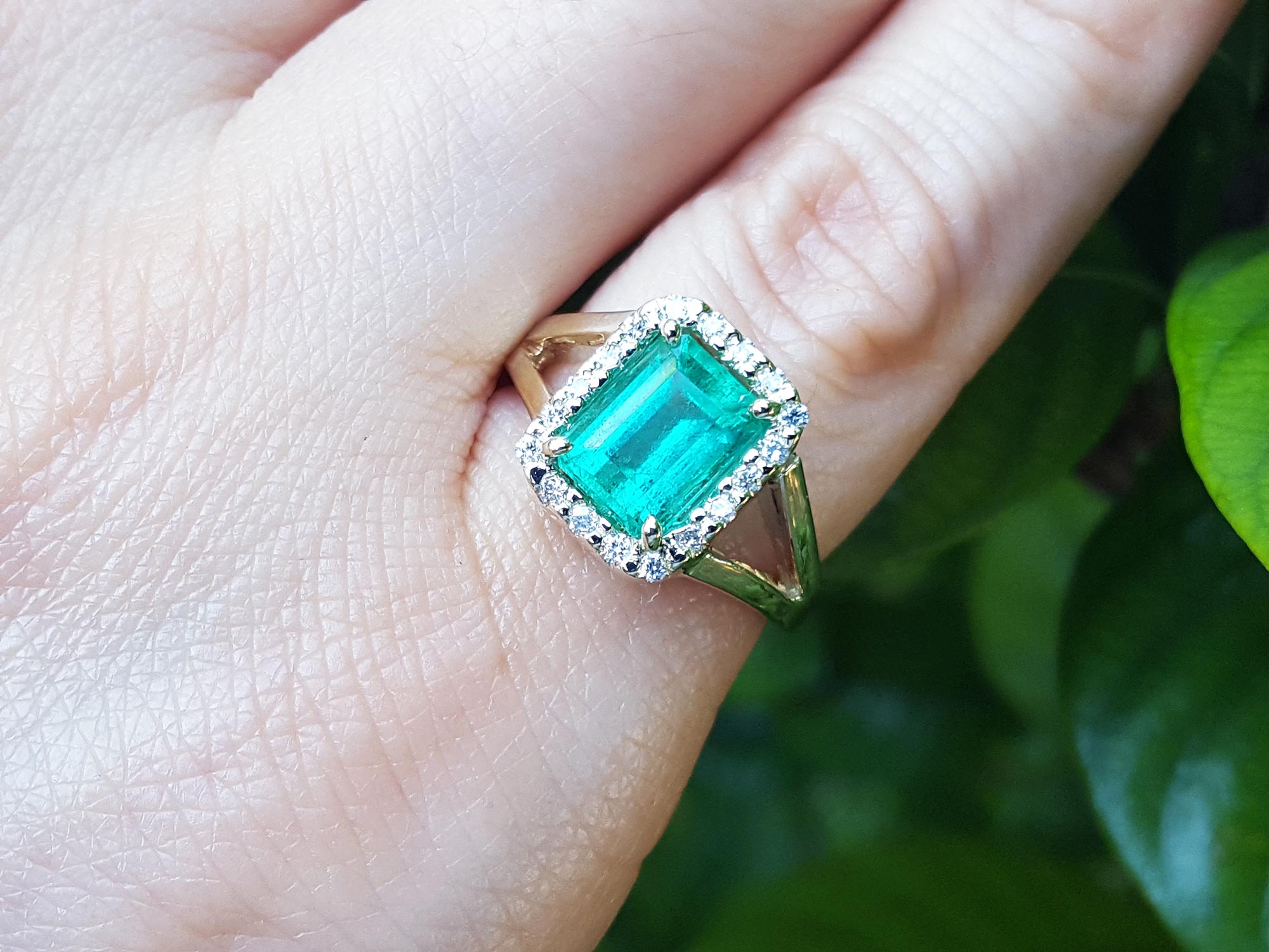 An emerald-cut emerald ring on a hand with a natural background.