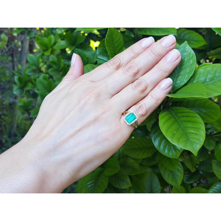 Emerald-cut Muzo Colombian emerald ring with diamond halo and split shank in 14k yellow gold on a hand.