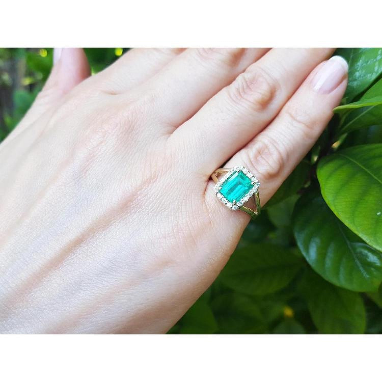 Emerald-cut Muzo Colombian emerald ring with diamond halo and split shank in 14k yellow gold on a hand.