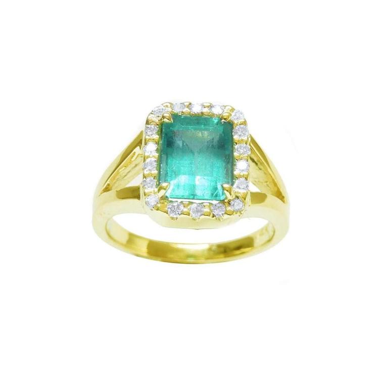 This emerald-cut Muzo Colombian emerald ring for women has a halo of natural diamonds and is crafted in 14k yellow gold.