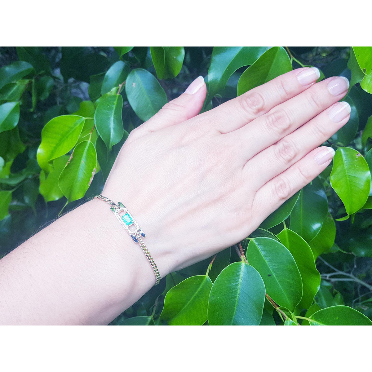 A woman&#39;s and wearing a natural Muzo colombian emerald bracelet with green leaves in the background.