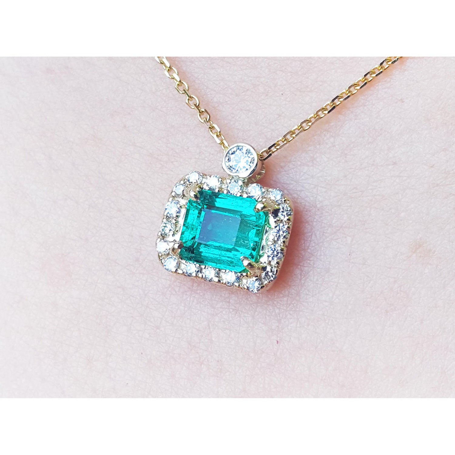 1.31 ct emerald-cut Muzo Colombian emerald necklace with diamond halo on 14K yellow gold chain.