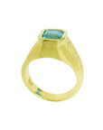 A lateral view of a men's yellow gold ring shows the top emerald bezel set and band design.