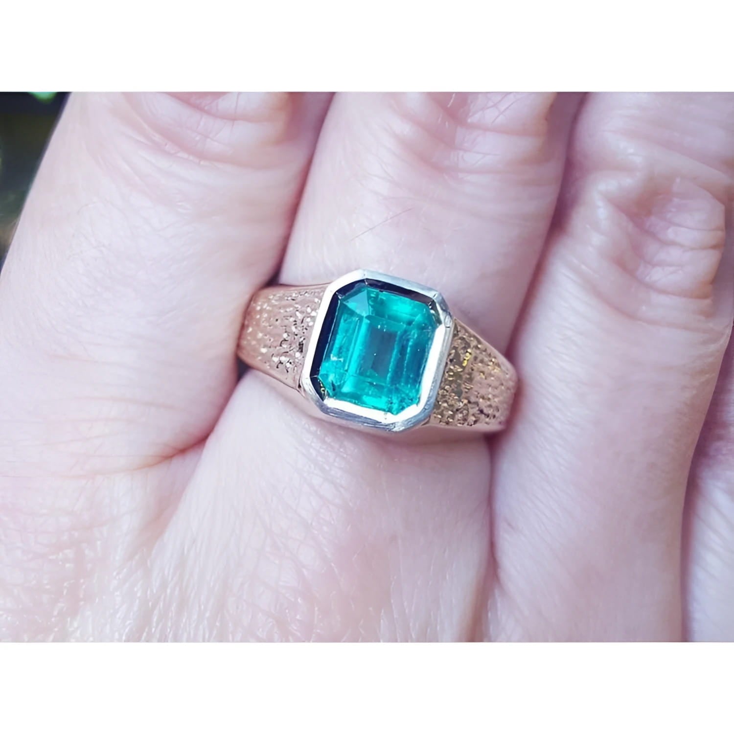 A 14k yellow gold men's ring with a natural Muzo colombian emerald bezel set worn on a finger.