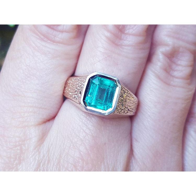 A 14k yellow gold men's ring with a natural Muzo colombian emerald bezel set worn on a finger.