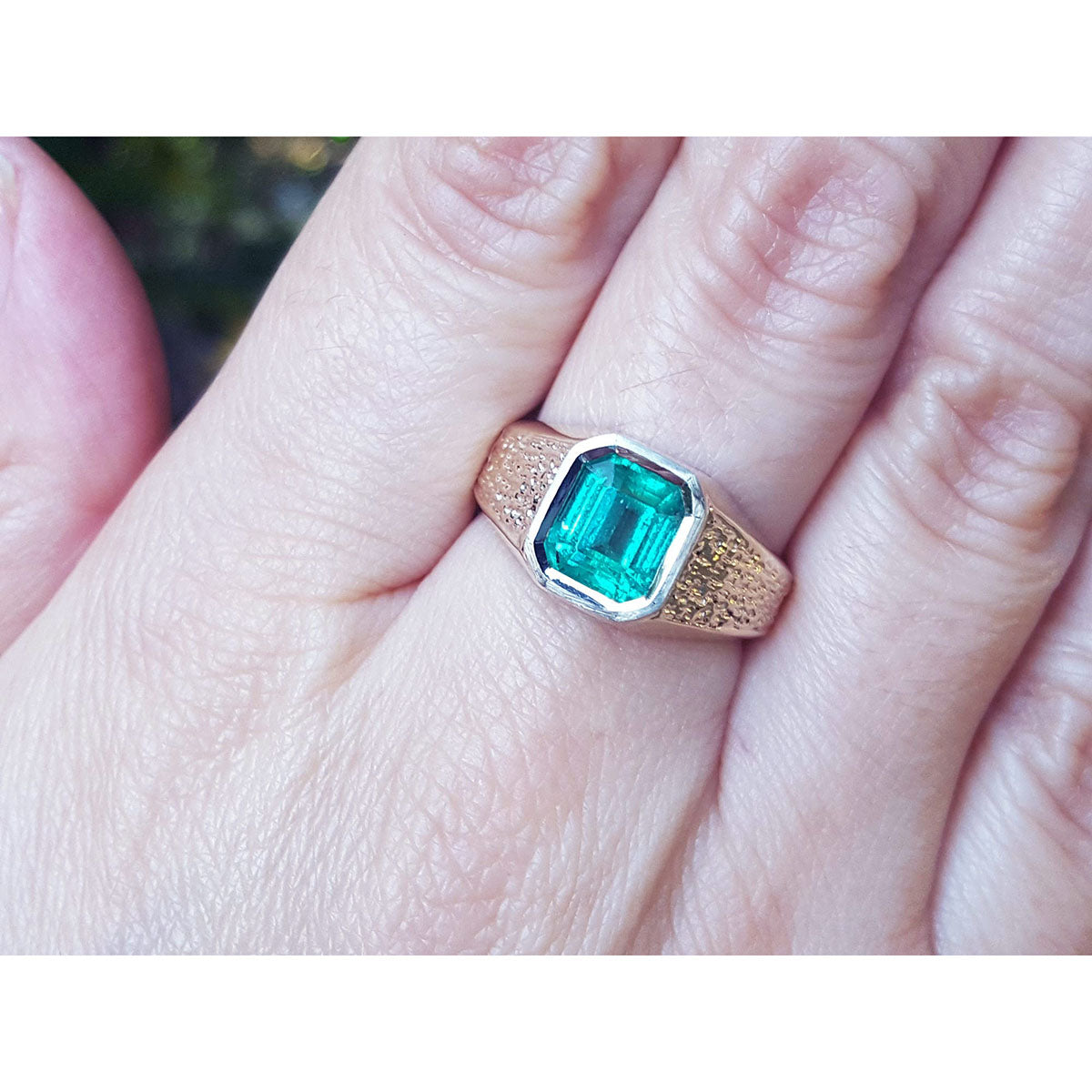 Gold ring for men with a bezel set natural colombian emerald on a finger.