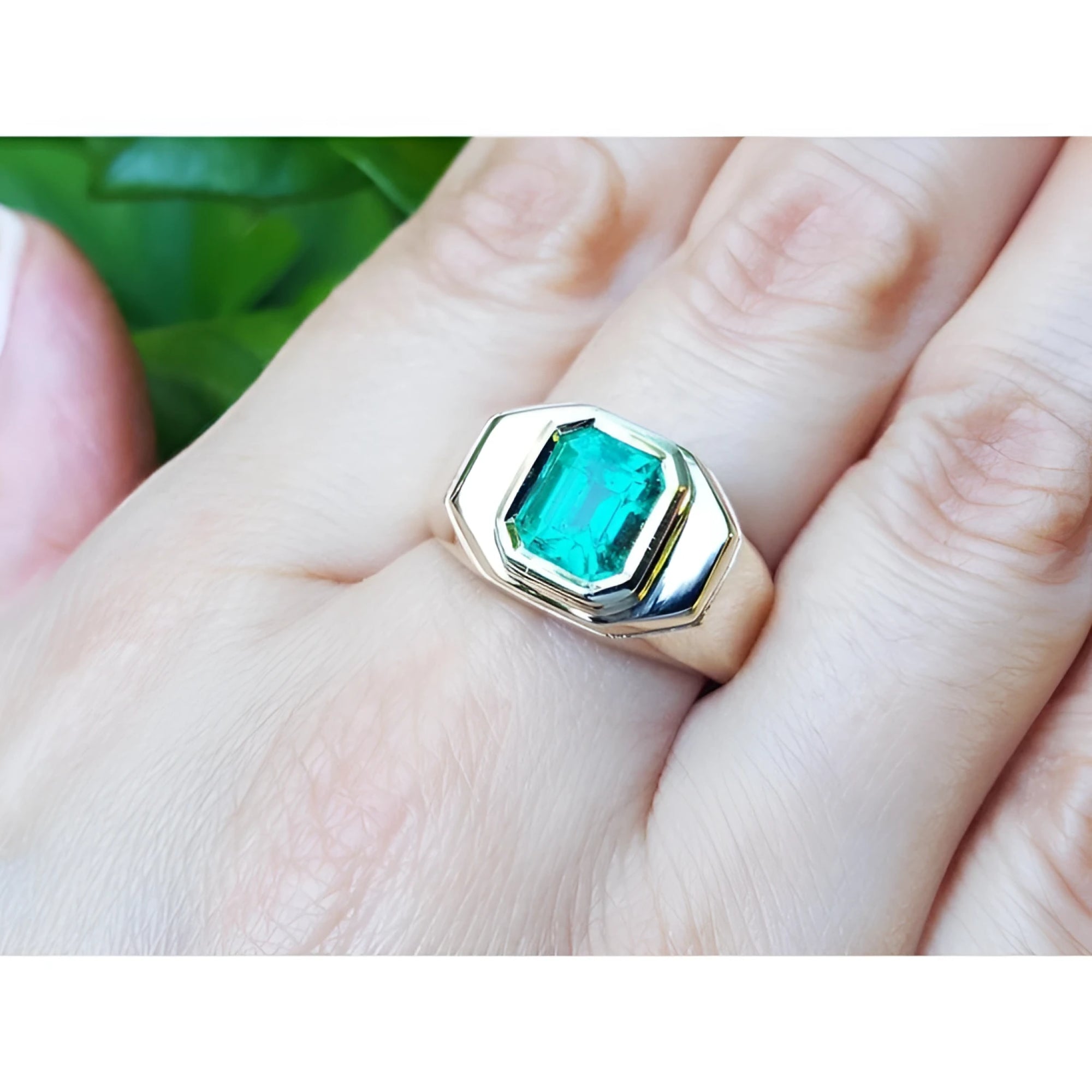 A 14k yellow gold ring for men with a bezel set square natural colombian emerald worn on a hand.